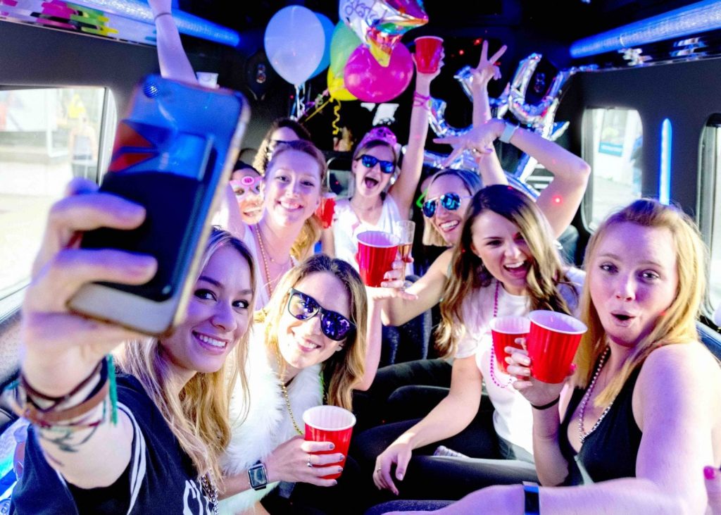 nine women on a party bus while woman in front holds up phone to take a selfie