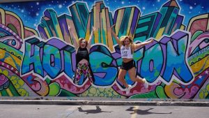 two women jumping in front of colorful houston mural