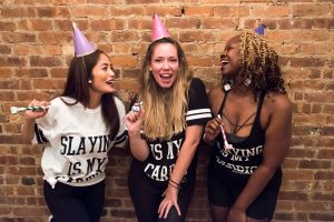 women celebrating birthday party in party hats in front of brick wall