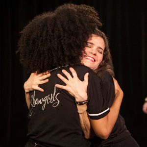 performance programs - two women hugging in front of a black background