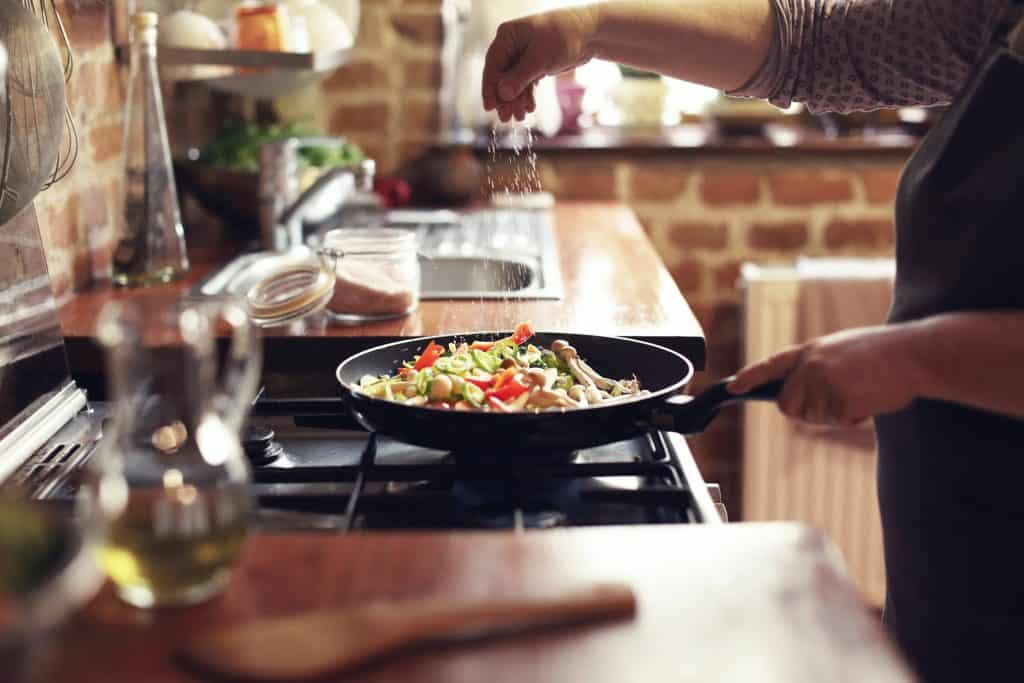 A Person Cooking Vegetables in a Pan on a Stove