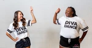 Two women wearing white DivaDance t-shirts high-fiving each other