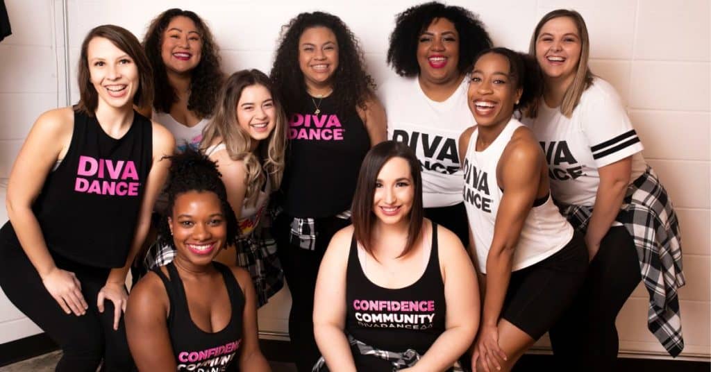 Nine diverse women in DivaDance t-shirts smiling and looking at the camera after a DivaDance class