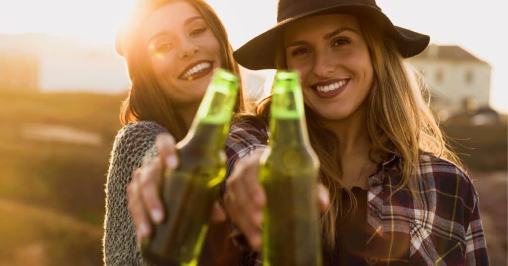 Two women toasting bottles of beer to the camera. 