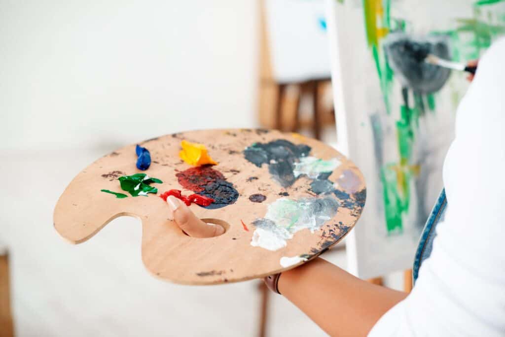 A woman holding a palette of paints in an art studio, showcasing one of the many creative things to do in Toledo.