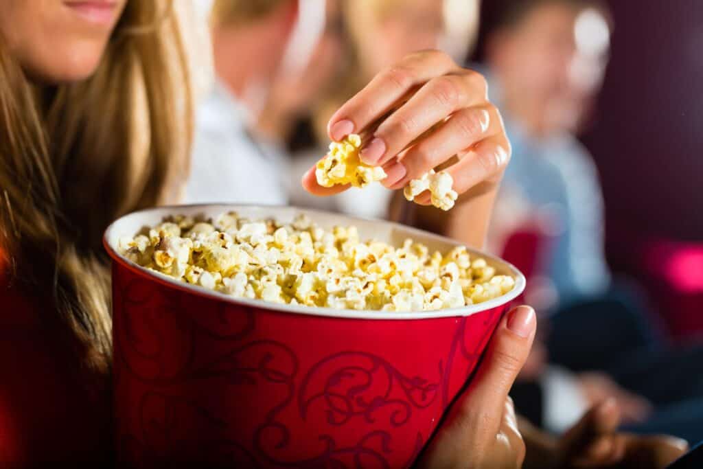 A person eating popcorn from a red bowl.