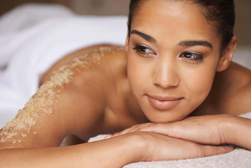 A woman laying on a towel with sand on her back at the spa.