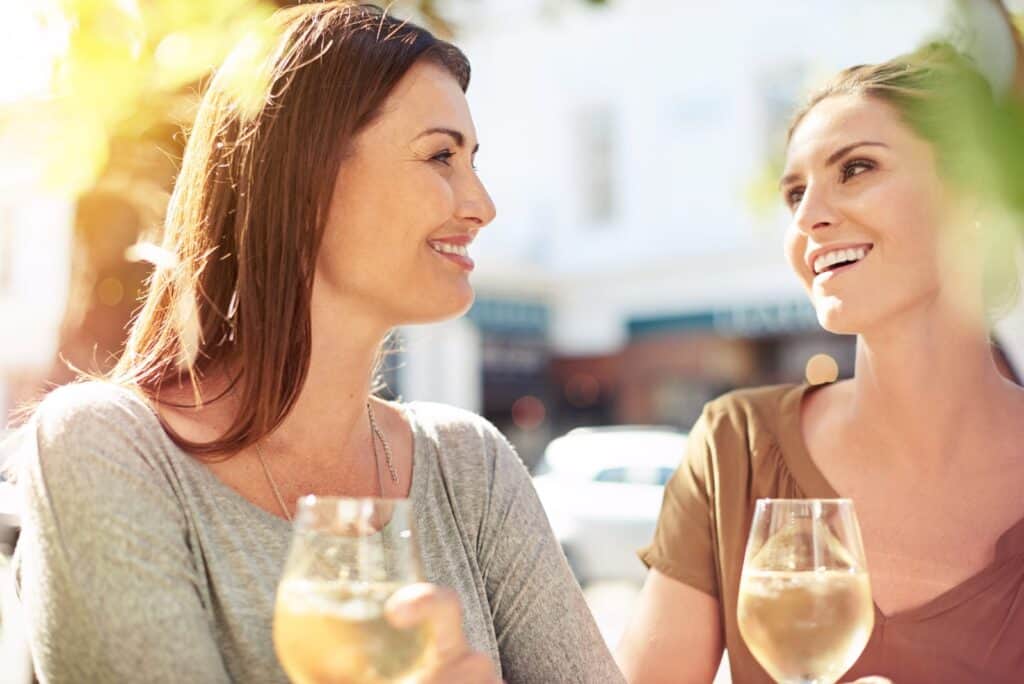 Two women holding wine glasses and smiling at each other.