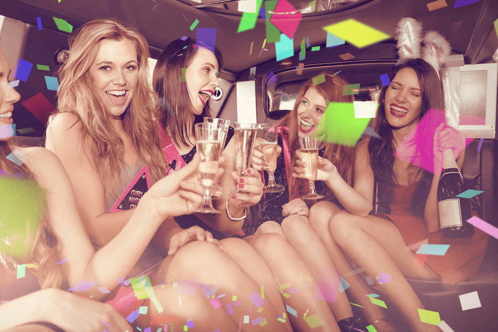 A group of women sitting in the back of a limo with confetti.