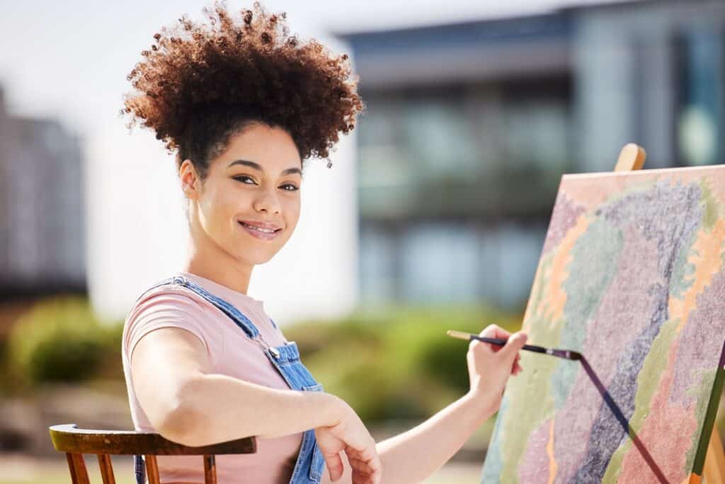 Young woman painting on a canvas outdoors.