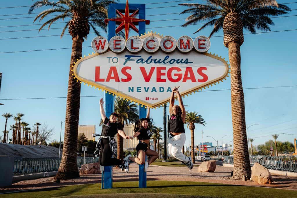 Three people joyfully jumping in front of the "welcome to fabulous las vegas" sign.