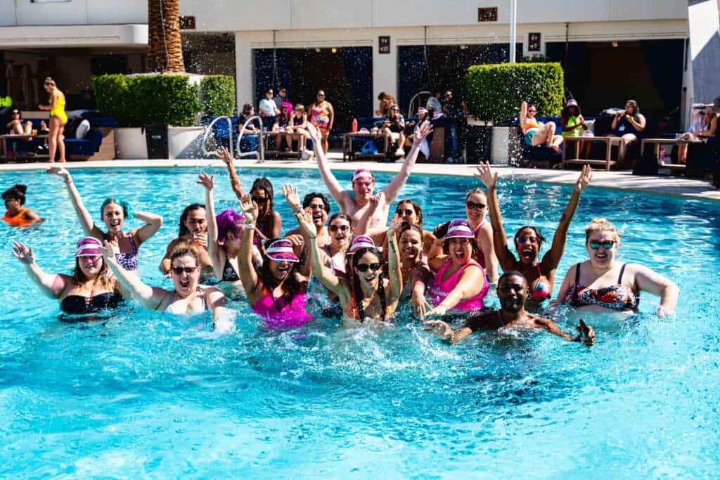 Group of people enjoying a pool party, enthusiastically posing with raised arms.