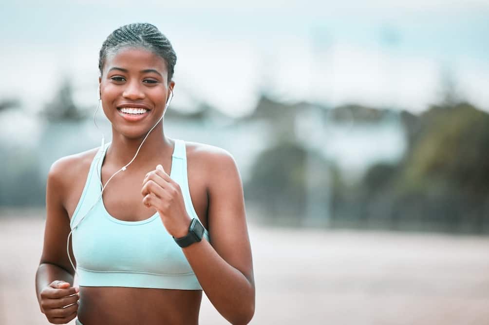 A smiling woman with headphones jogging outdoors.