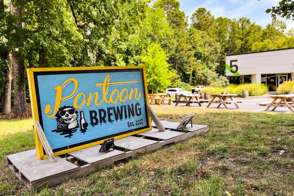 A colorful pontoon brewing company sign placed outdoors with picnic tables in the background.