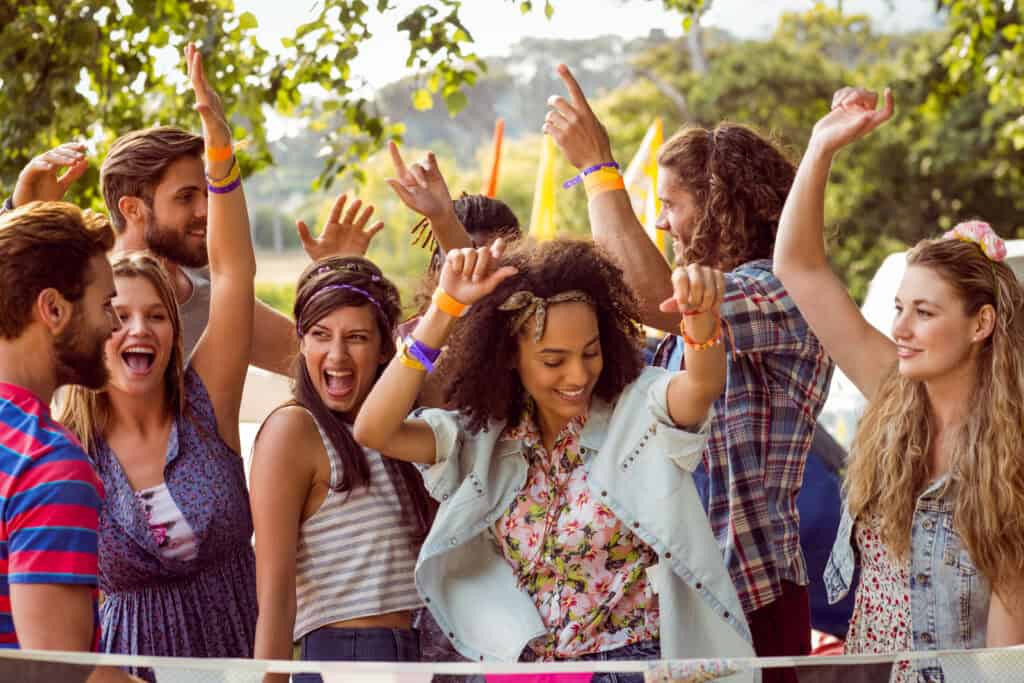 A group of people enjoying an outdoor party, some with hands raised and others laughing or smiling, under a tree — perfect inspiration for bachelorette party ideas in Northwest Arkansas.